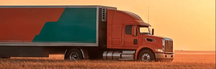 Red semi-truck driving on a highway at sunset